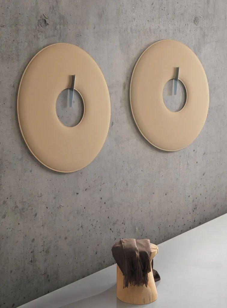 Zwei runde Akustikpaneele an Betonwand, jeweils mit integrierter Kleideraufhängung, daneben steht ein Holzschemel mit Schal.