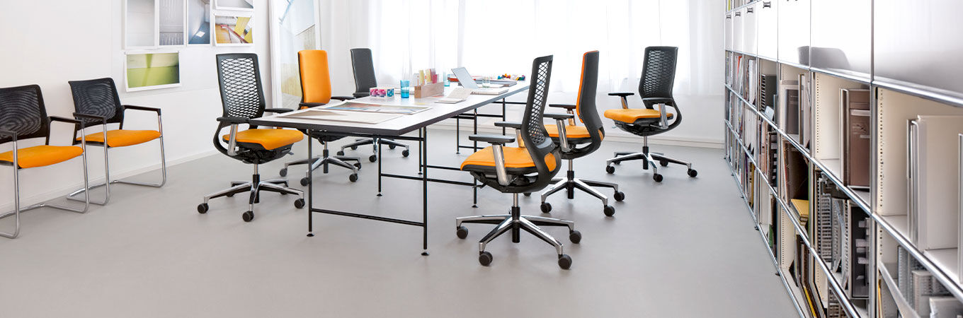 Moderner Büroraum mit ergonomischen Stühlen in Schwarz und Orange um einen großen Tisch herum.