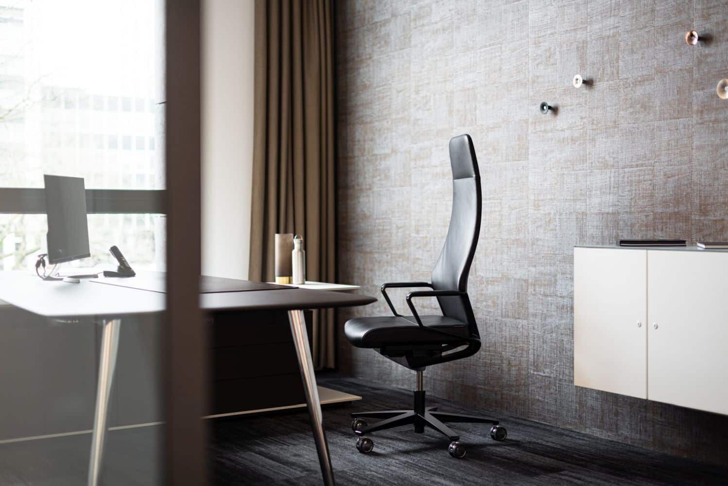 Hochwertiger ergonomischer Bürostuhl in modernem, hellem Büro mit elegantem Schreibtisch und grauer Wandgestaltung.