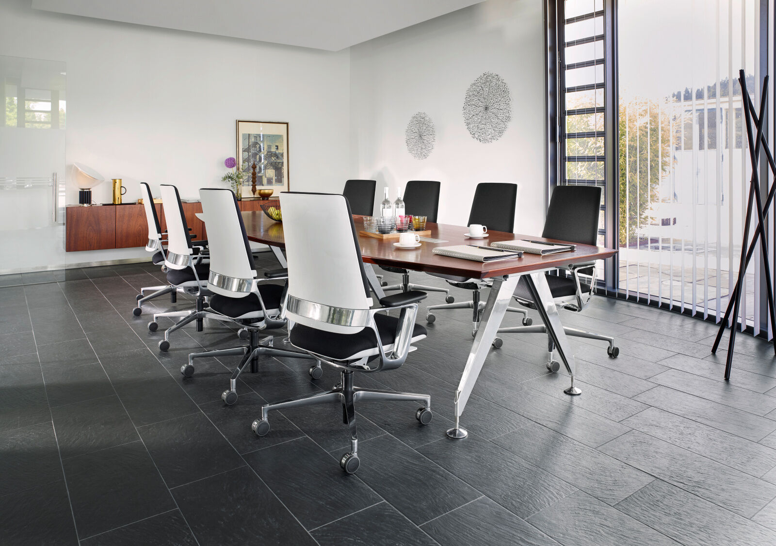 Moderner Konferenzraum mit ergonomischen Drehstühlen um einen Holztisch, Fenster mit Jalousien rechts.