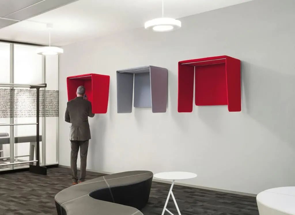 Mann steht an einer Wand, spricht in eine rote Wandtelefonzelle in einem modernen Büro.