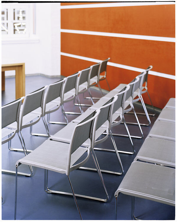Reihen von modernen Stühlen in einem Konferenzraum mit oranger Wand und blauen Boden.