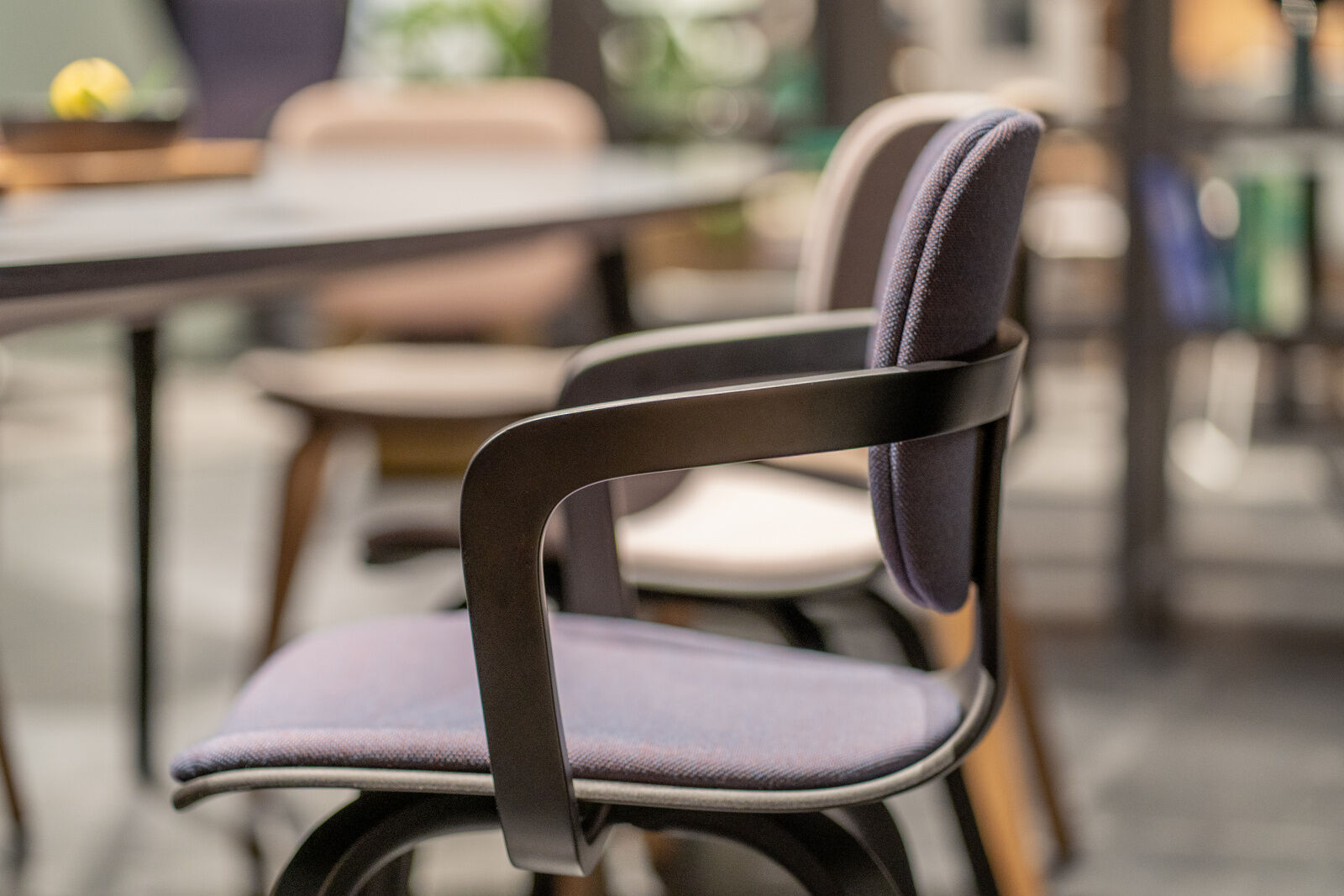 Ergonomischer Bürostuhl mit schwarzen Armlehnen, lila Stoffbezug, im Fokus eines modernen Büroambientes.