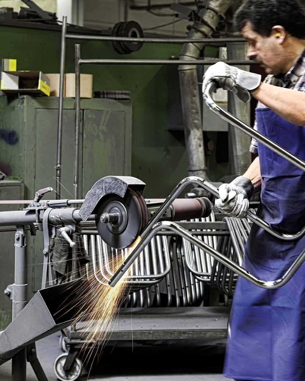 Arbeiter schleift Metallstuhlgestell, Funken fliegen. Fördert die Qualität von ergonomischen Bürostühlen bei Chairgo.