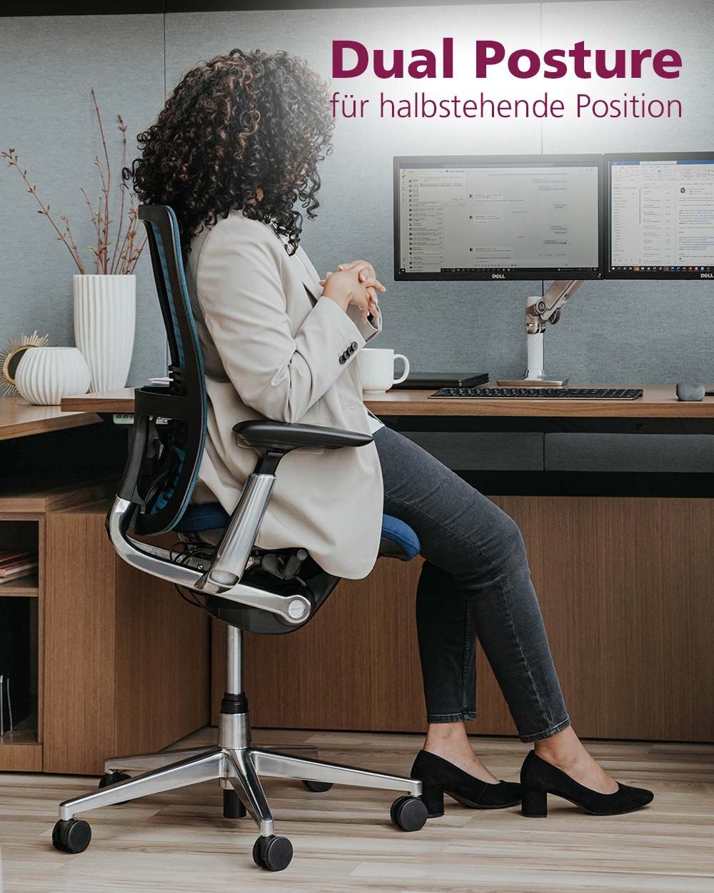 Frau sitzt auf ergonomischem Bürostuhl vor Schreibtisch mit zwei Monitoren, bewirbt halbsitzende Haltung.