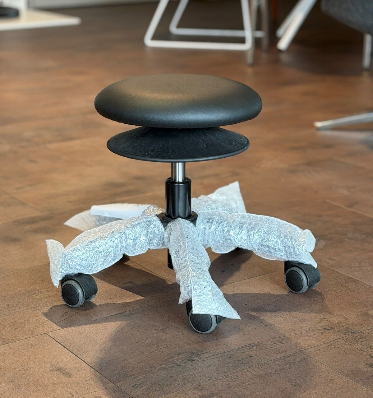 Moderner ergonomischer Bürohocker mit Rundsitzfläche und Rollen, noch teilweise in Schutzfolie verpackt.