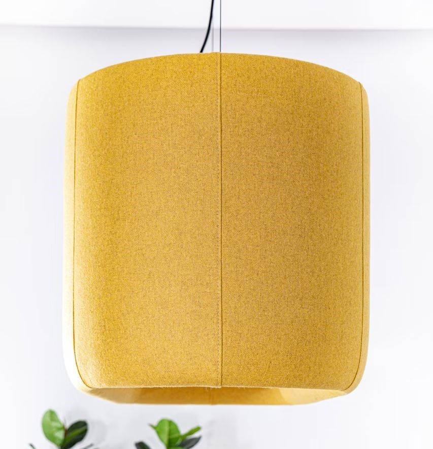 Gelber, moderner Lampenschirm in Nahaufnahme, mit einzelnen Pflanzenblättern am unteren Bildrand sichtbar.