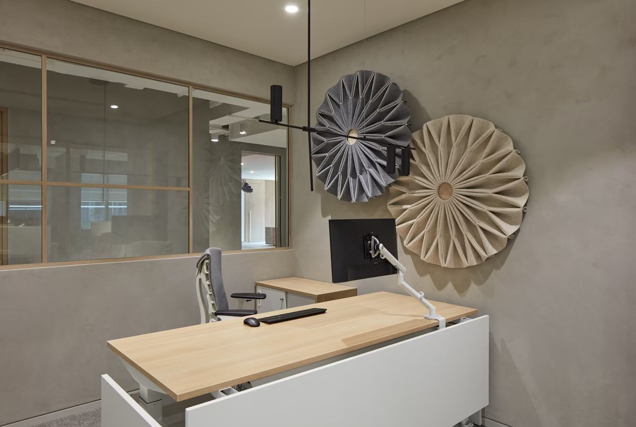 Modernes Büro mit ergonomischem Stuhl, Holzschreibtisch und abstrakten Wanddekorationen in neutralen Tönen.
