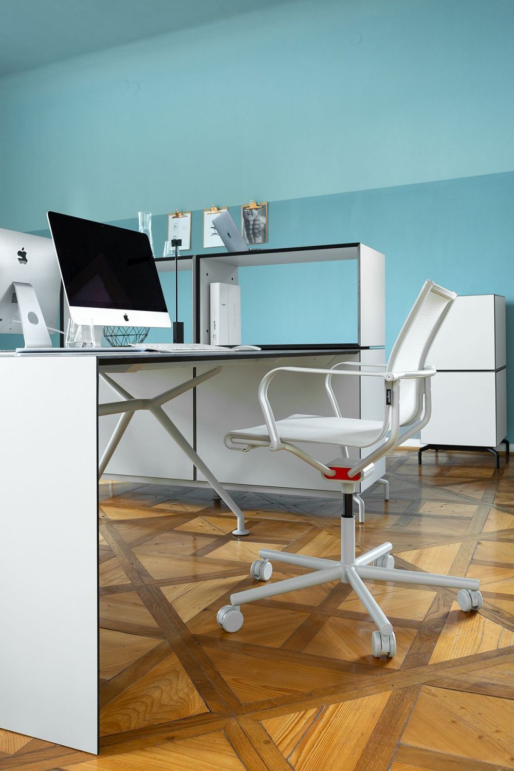 Moderner Home-Office-Arbeitsplatz mit ergonomischem weißem Bürostuhl und schlichter weißer Schreibtisch, blauer Wandhintergrund.