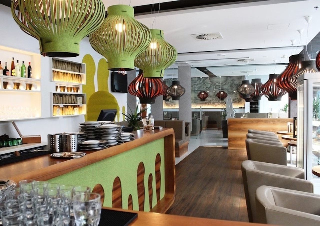 Modernes Restaurant mit grünen und braunen Lampen, Barbereich und komfortablen Sitzgelegenheiten aus Holz.