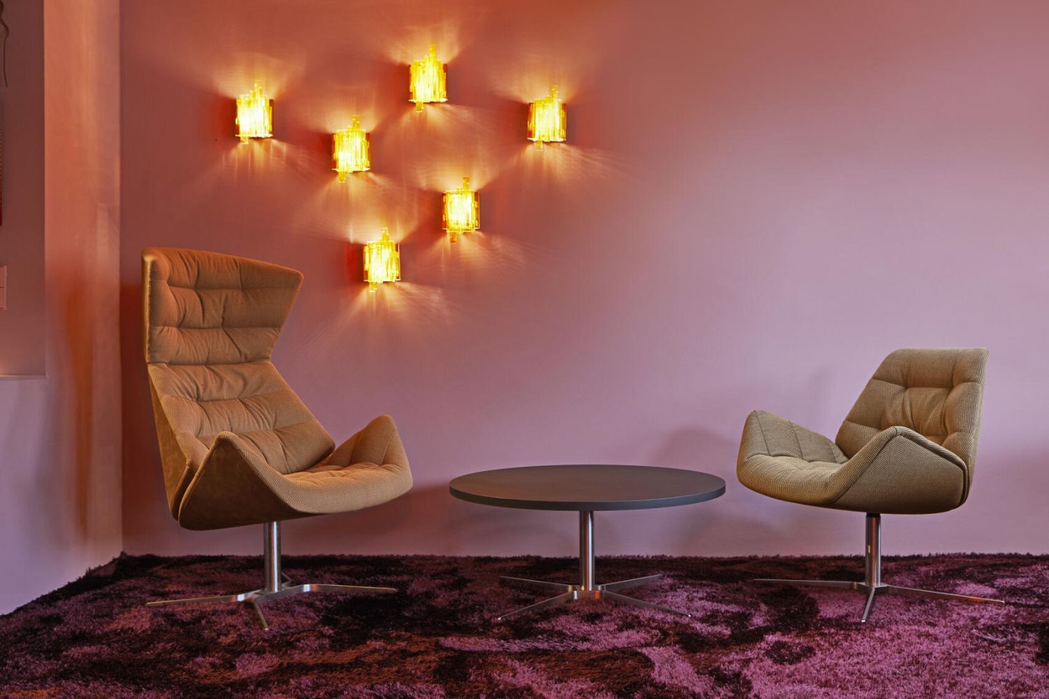 Zwei ergonomische Stühle und ein runder Tisch vor einer rosa Wand mit stilvoller Beleuchtung.