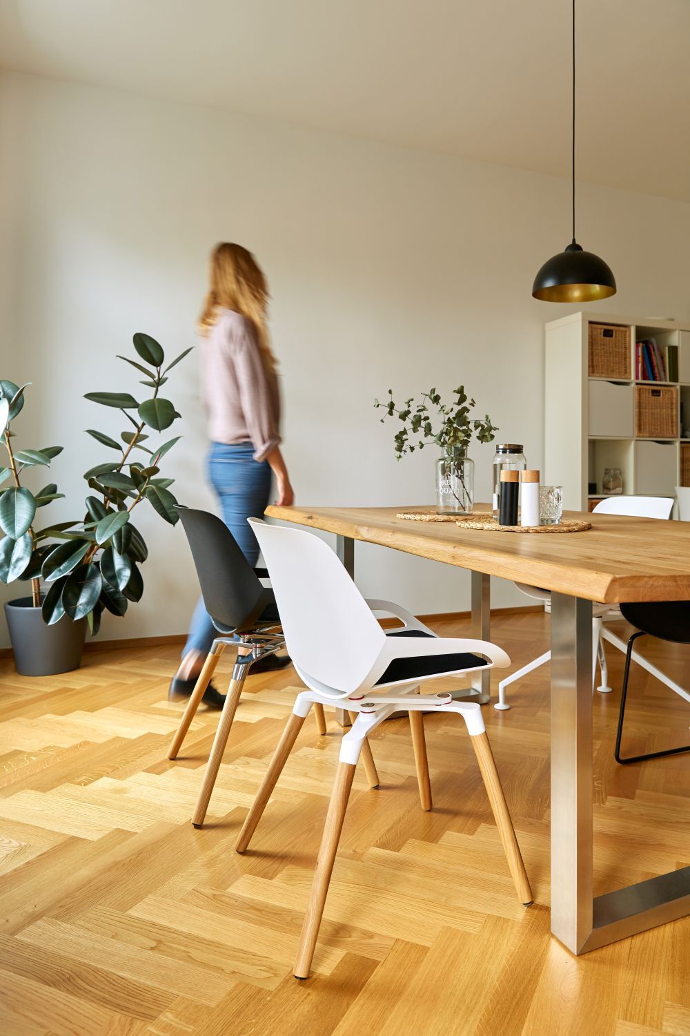 Moderner Essbereich mit stilvollen Stühlen, Holztisch und großen Pflanzen im Wohnraum, Person in Bewegung.