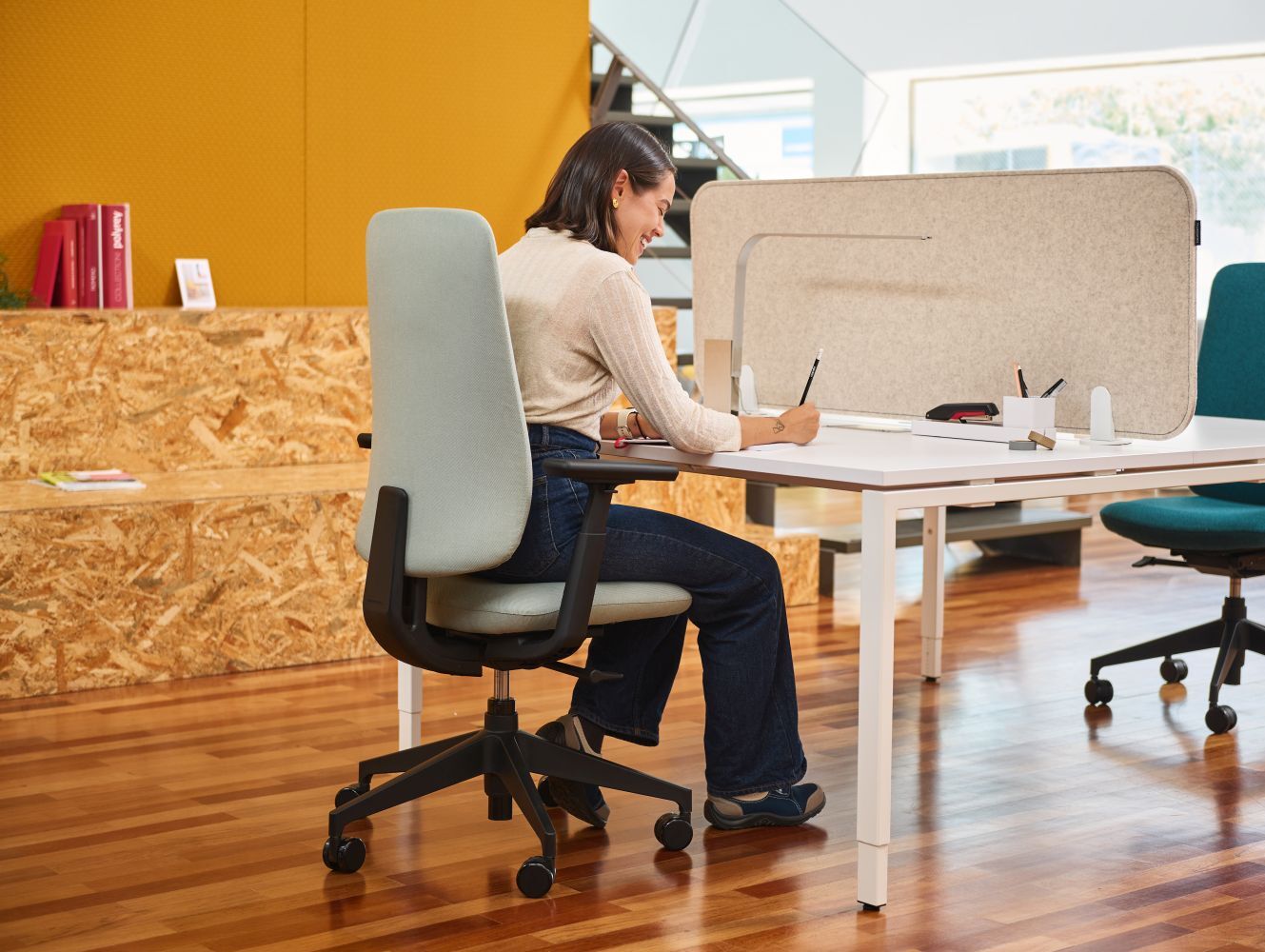 Frau sitzt dynamisch auf einem ergonomischen Bürostuhl und arbeitet konzentriert an einem modernen Schreibtisch.