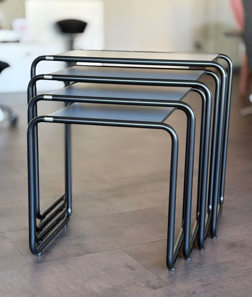 Vier stapelbare, schwarze, minimalistische Tische in einem modernen Büro auf einem Holzboden arrangiert.