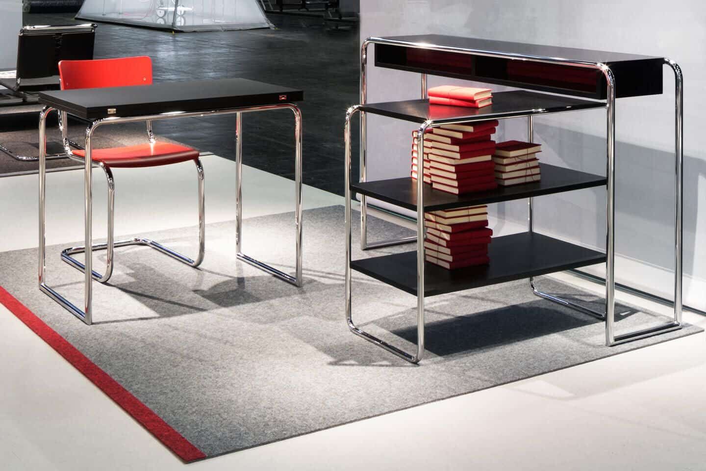 Ergonomische Büromöbel mit verchromtem Gestell, rotem Stuhl und Regal voller Bücher auf grauem Teppich.