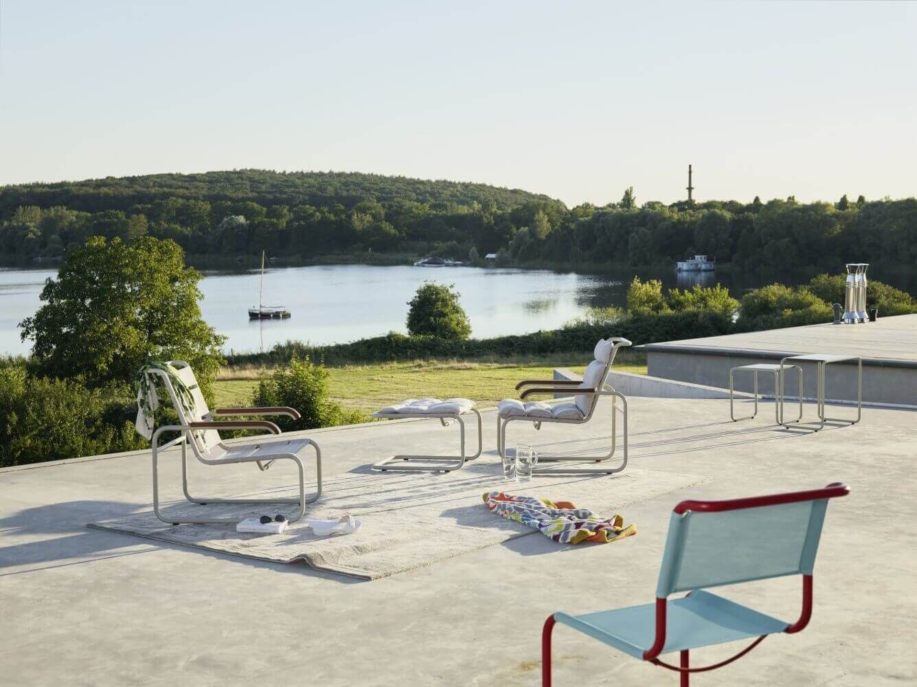 Ergonomische Stühle auf einer Terrasse mit Seeblick, umgeben von grüner Landschaft und klarem Himmel.
