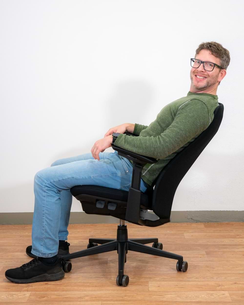 Mann sitzt lächelnd auf ergonomischem Bürostuhl mit flexibler Rückenlehne in entspannter Haltung.