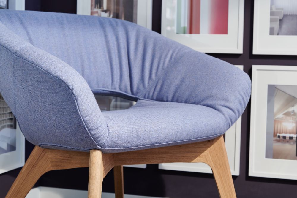 Moderner blauer Stuhl mit Holzbeinen vor einer Galerie von gerahmten Bildern an der Wand.