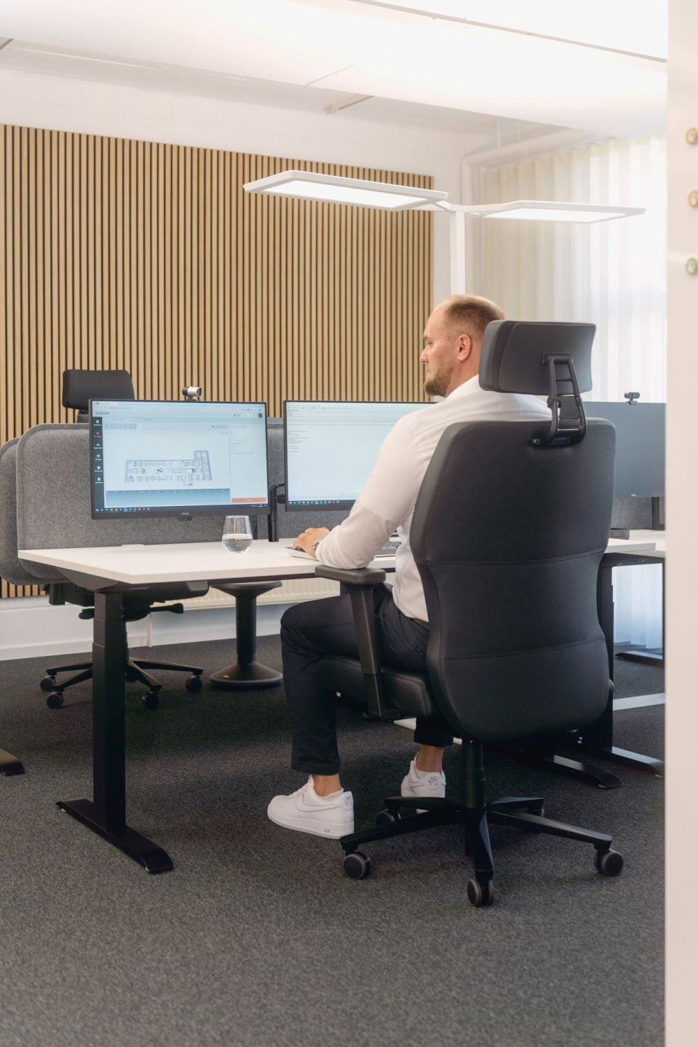 Mann sitzt auf ergonomischem Bürostuhl vor mehreren Bildschirmen in modernem Büro, betont Arbeitsplatzgesundheit.