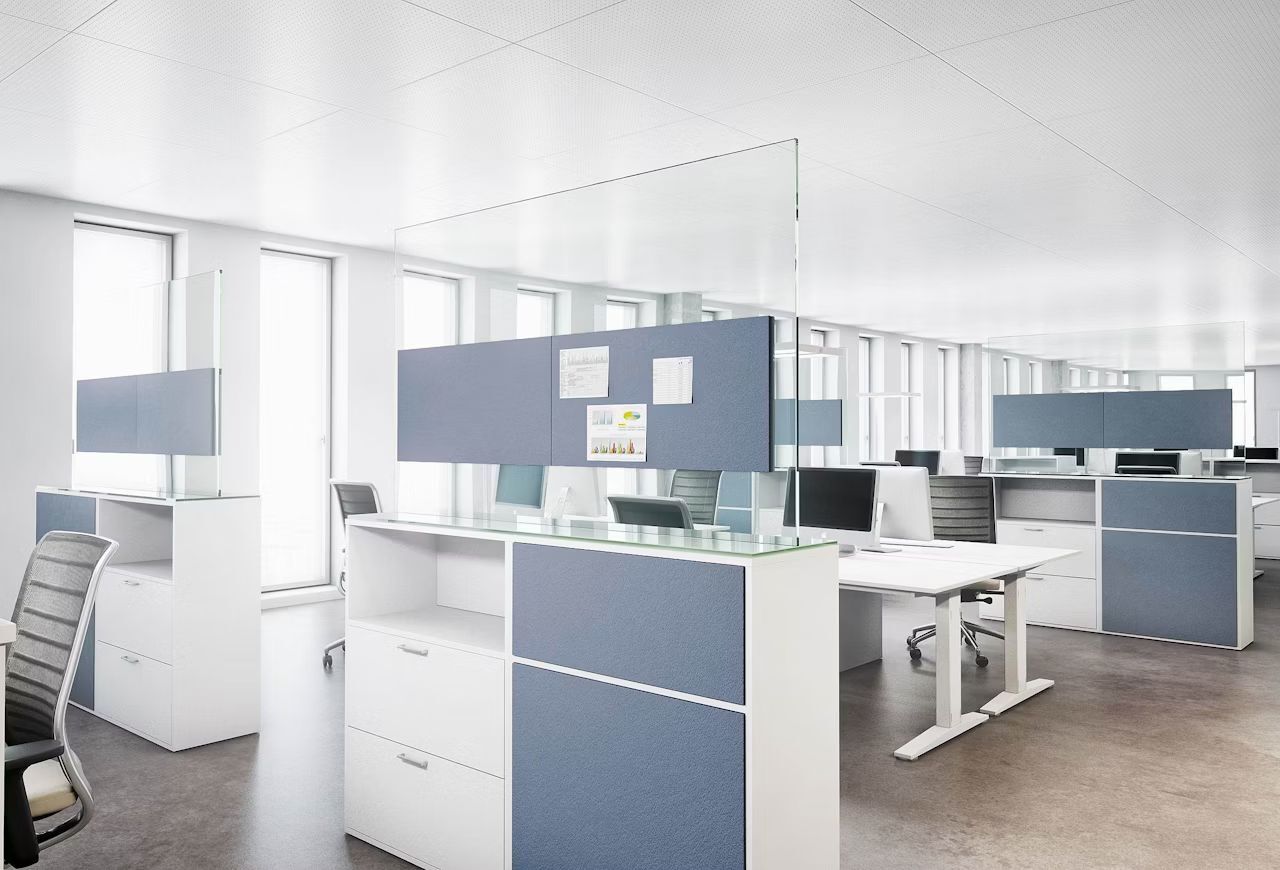 Modernes Büro mit ergonomischen Stühlen, weißen Tischen und Glas-Trennwänden für eine helle, produktive Umgebung.