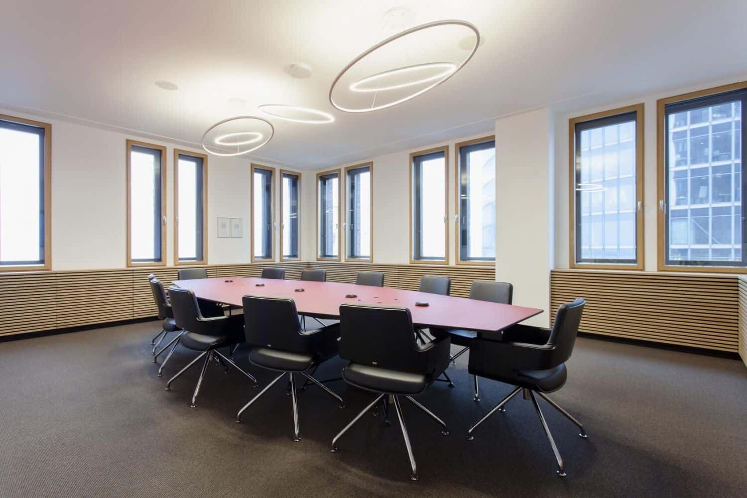 Moderner Konferenzraum mit ergonomischen Stühlen um einen großen, ovalen Tisch unter eleganter Beleuchtung.