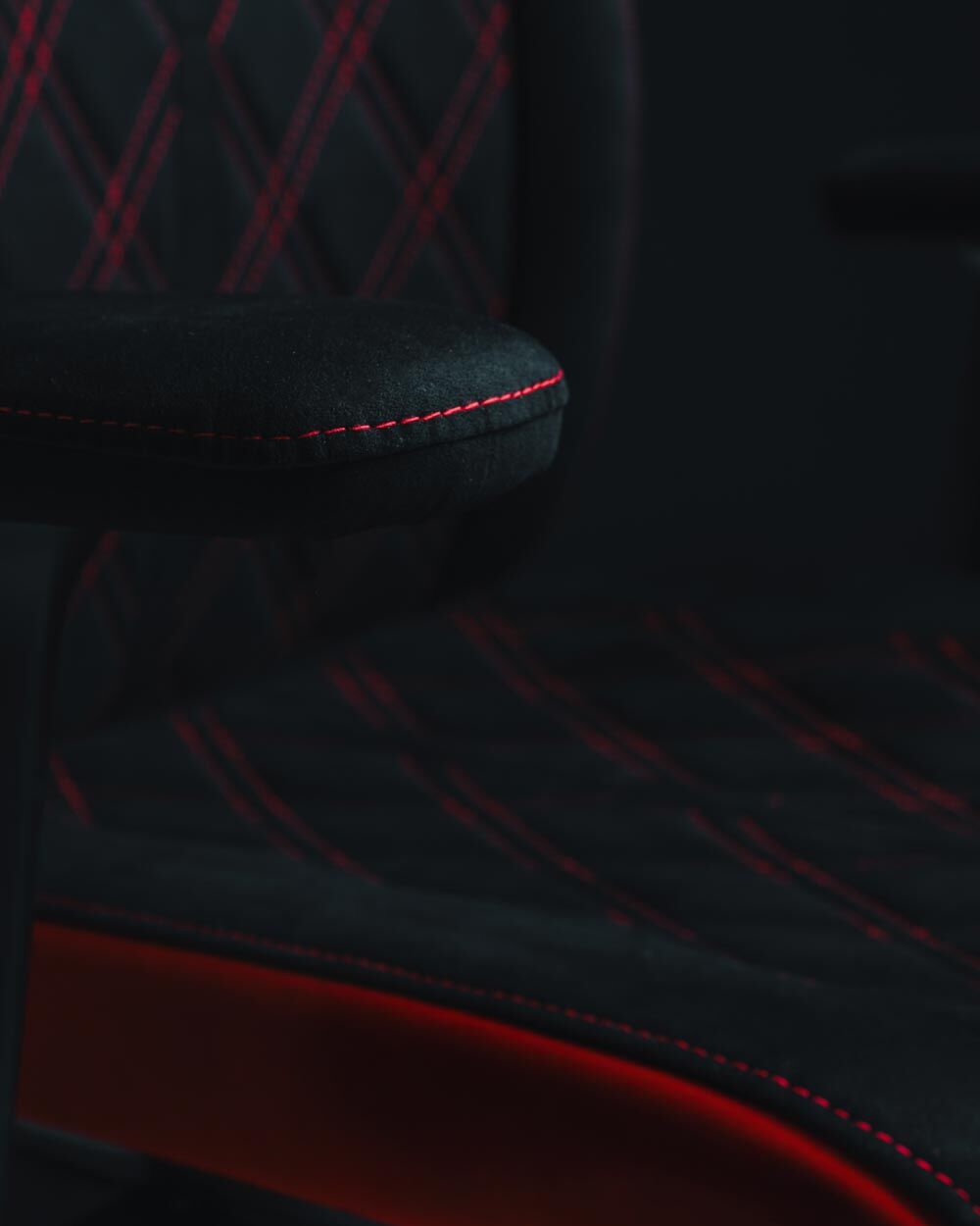 Nahaufnahme eines ergonomischen Stuhls mit schwarzem Bezug und roten Nähten, Fokus auf Details und Qualität.