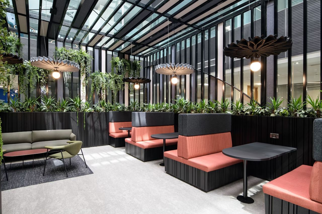 Modernes Bürodesign mit ergonomischen Sitzgelegenheiten, Pflanzenwand und natürlichem Licht für eine gesunde Arbeitsumgebung.