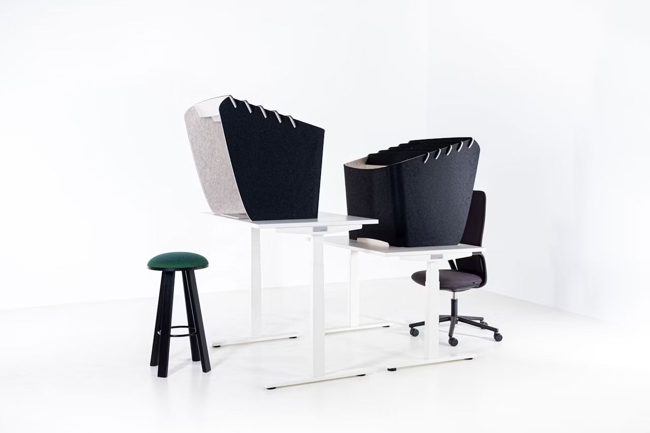 Zwei ergonomische Schreibtische mit Sichtschutz, ein Drehstuhl und ein grüner Hocker in minimalistischem Raum.