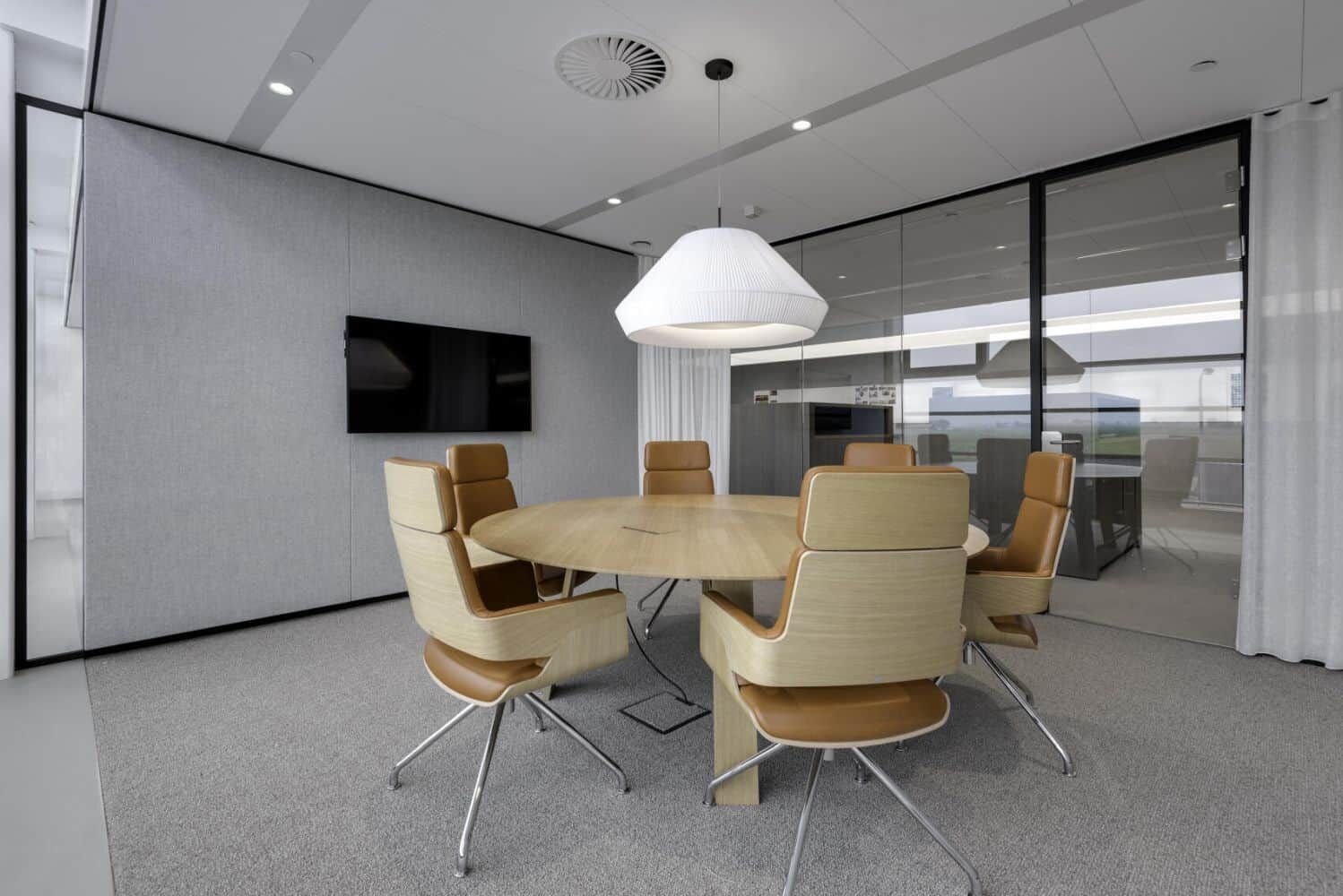 Moderner Konferenzraum mit rundem Holztisch, sechs ergonomischen Stühlen und stilvollem Hängeleuchter.