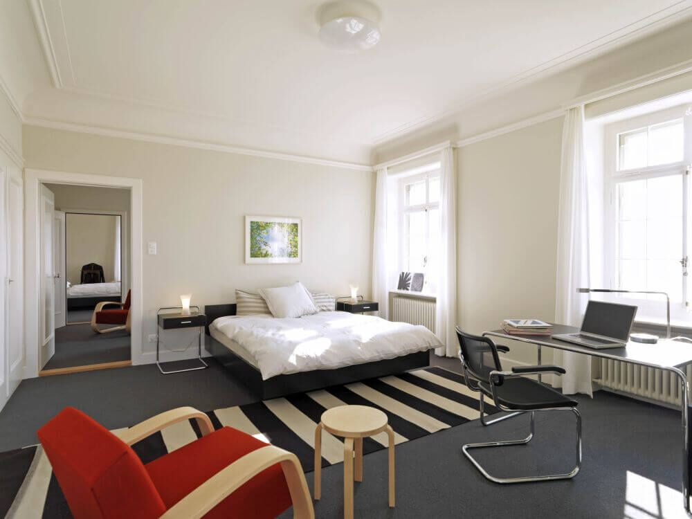 Geräumiges, helles Schlafzimmer mit modernen Möbeln, ergonomischem Bürostuhl, Schreibtisch und gemütlichem Bett.