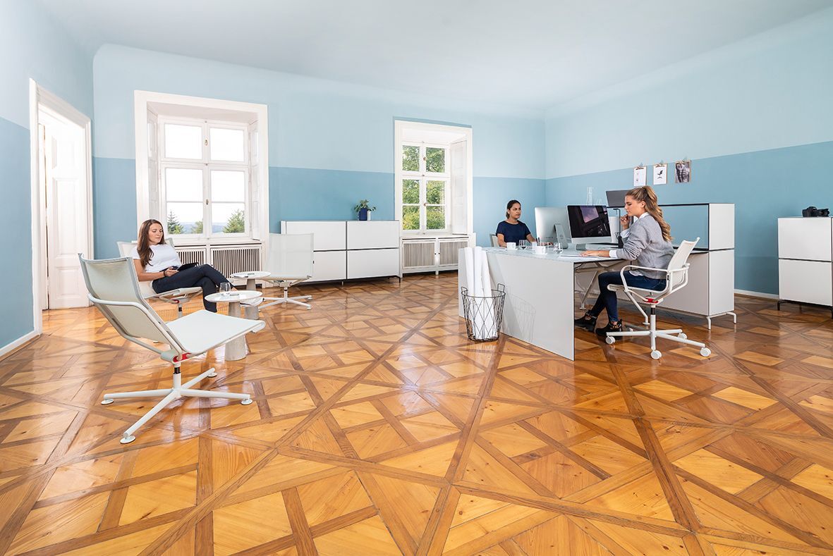 Modernes Büro mit ergonomischen Stühlen und hellem Interieur, drei Personen arbeiten und entspannen sich.