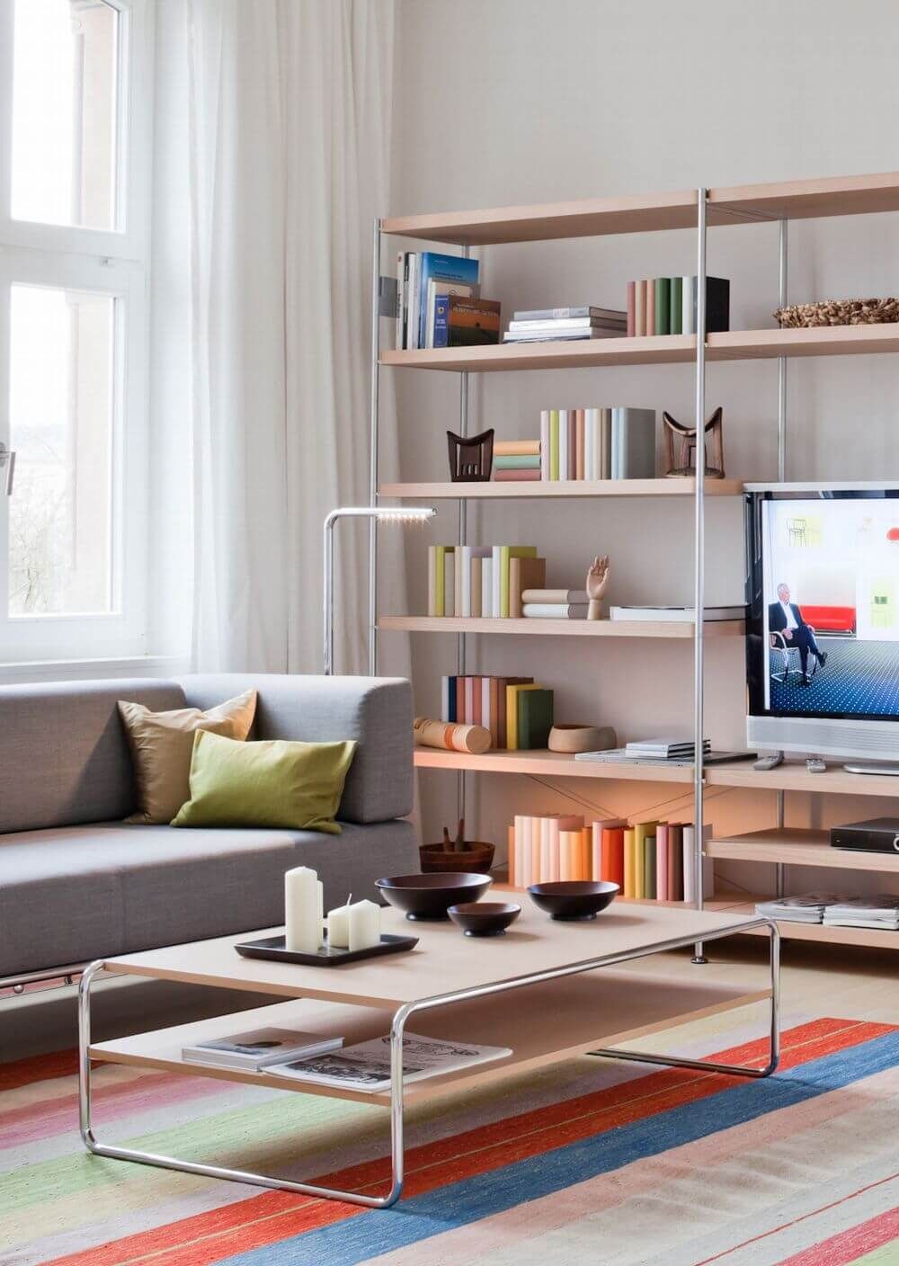 Elegantes Wohnzimmer mit grauem Sofa, Regalen mit Büchern und modernem Couchtisch auf farbigem Teppich.