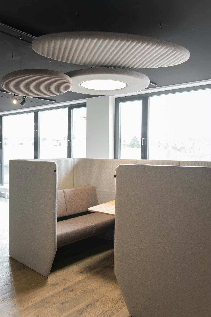 Moderner Besprechungsraum mit beigen Wänden, Holzboden und stilvollen, runden Akustikdeckenpaneelen.