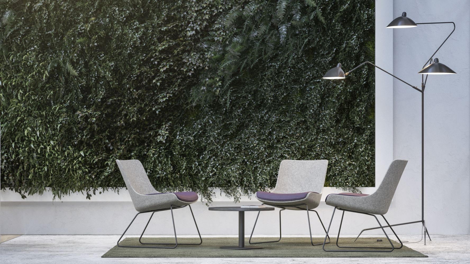 Drei ergonomische Stühle um einen Tisch vor einer grünen Pflanzenwand, beleuchtet von einer Stehlampe.