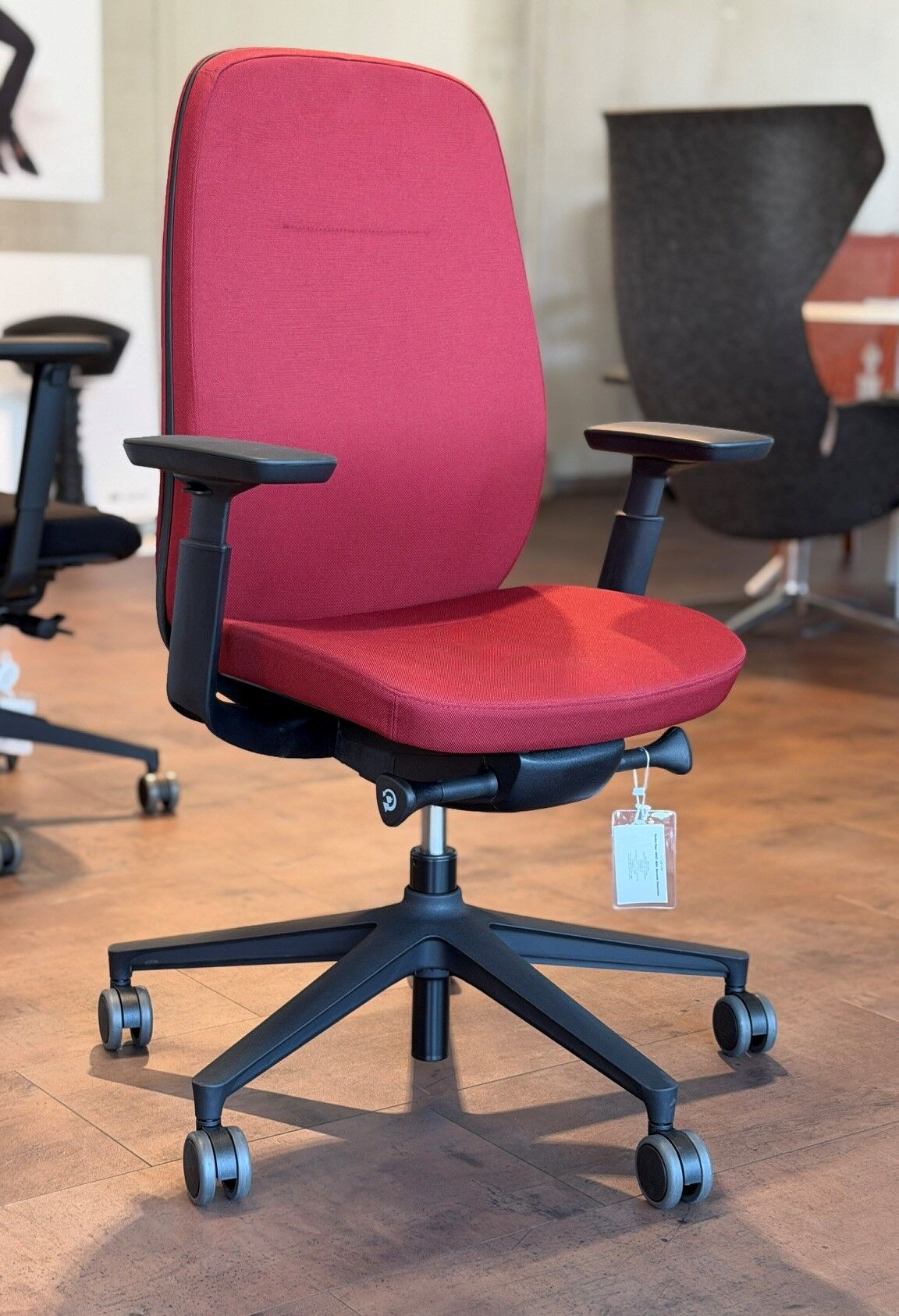 Roter ergonomischer Bürostuhl mit verstellbaren Armlehnen auf einem Holzfußboden in einem modernen Büro.