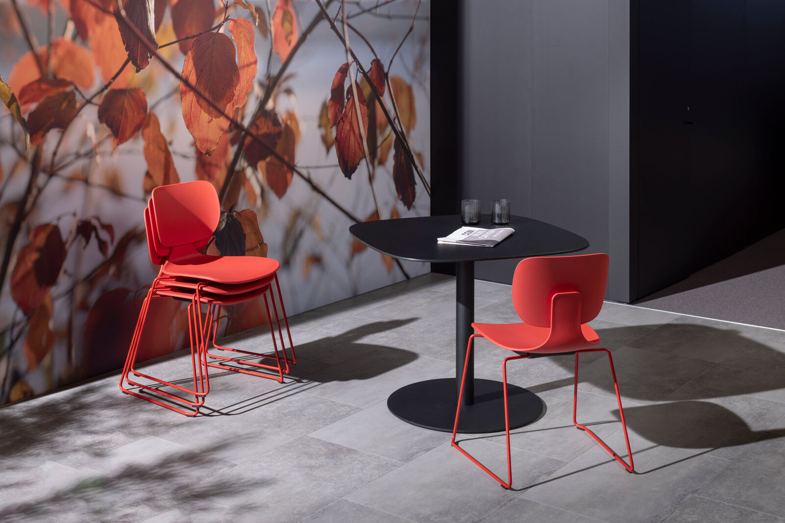 Rote Stühle an einem schwarzen Tisch vor einer Wand mit herbstlichem Blättermotiv in moderner Büroeinrichtung.