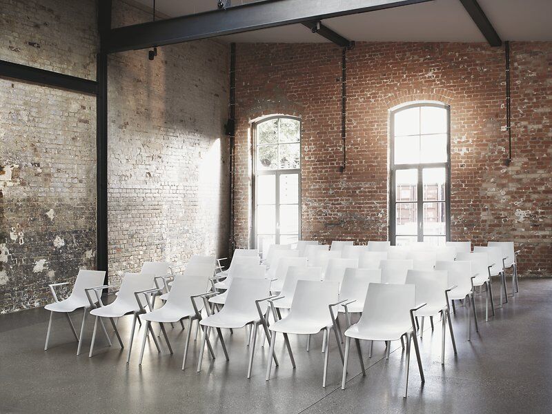 Weiße ergonomische Stühle in einem Raum mit Backsteinmauern und großen Fenstern, ideal für dynamisches Sitzen.