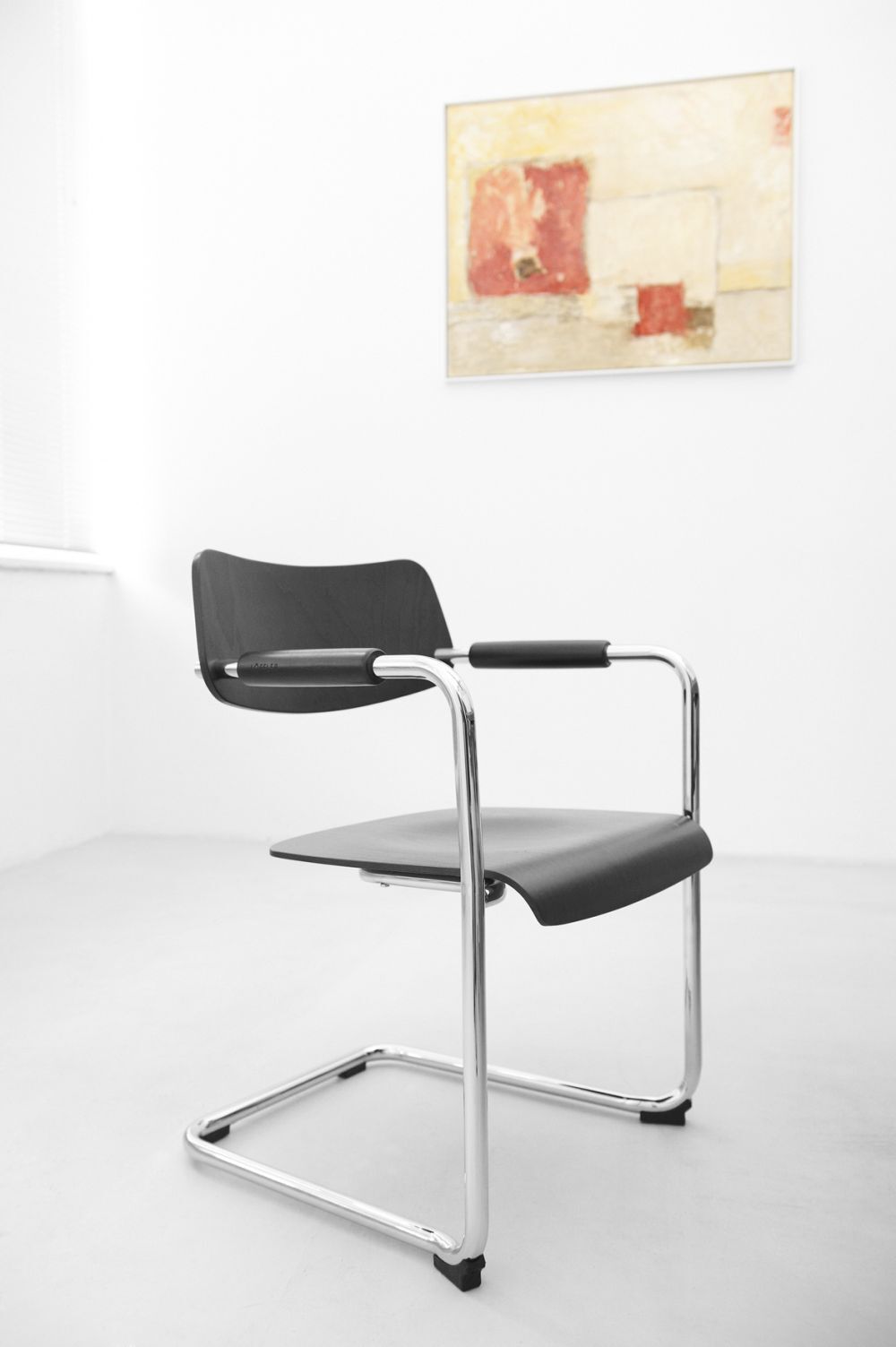 Moderner schwarzer Bürostuhl mit Chromrahmen vor einem abstrakten Gemälde in einem minimalistisch gestalteten Raum.