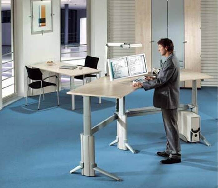 Mann im Anzug steht an einem ergonomischen höhenverstellbaren Schreibtisch mit zwei Monitoren im modernen Büro.