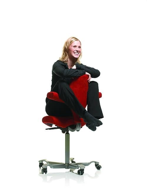 Frau sitzt entspannt auf einem ergonomischen roten Drehstuhl, der dynamisches Sitzen fördert.