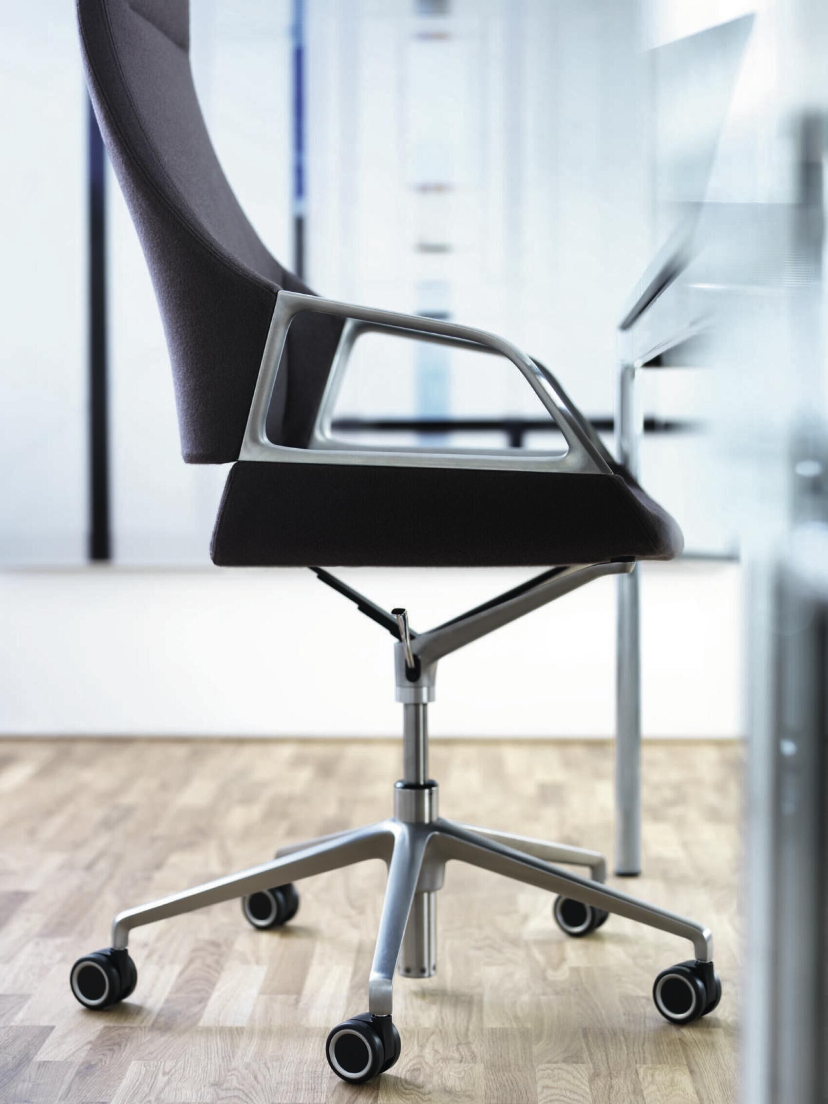 Seitliche Ansicht eines ergonomischen Bürostuhls mit hoher Rückenlehne und Rollen auf Holzfußboden.