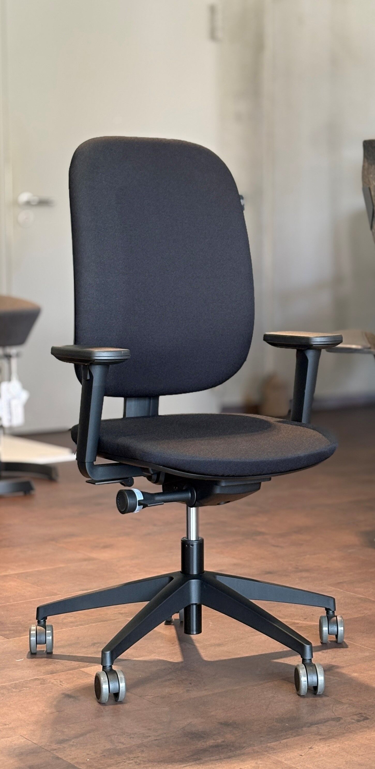 Ergonomischer Bürostuhl mit schwarzem Stoffbezug und verstellbaren Armlehnen auf Rollen, ideal für dynamisches Sitzen.