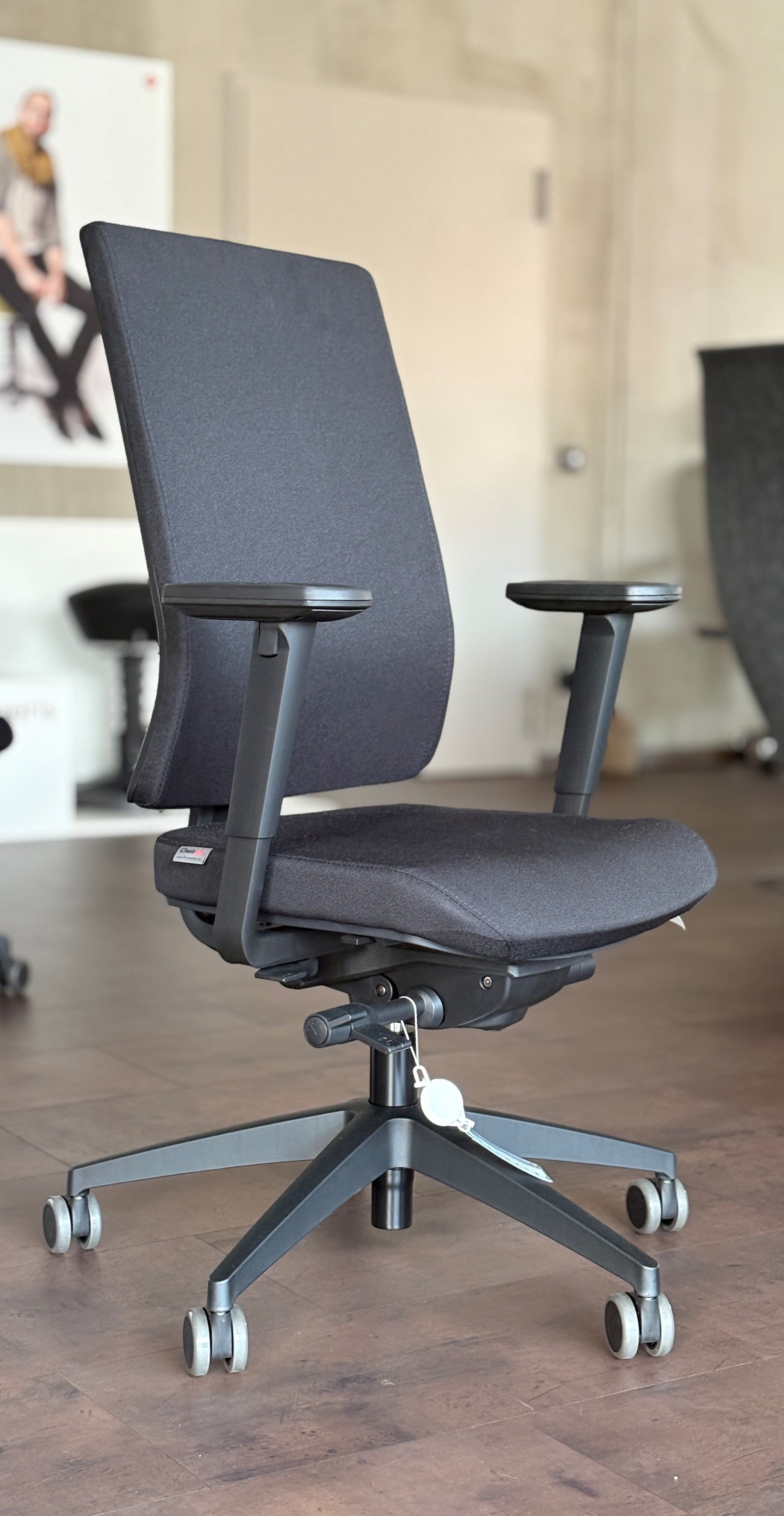 Moderner schwarzer Bürostuhl mit ergonomischen Armlehnen und Rollen auf Holzboden im Showroom ausgestellt.