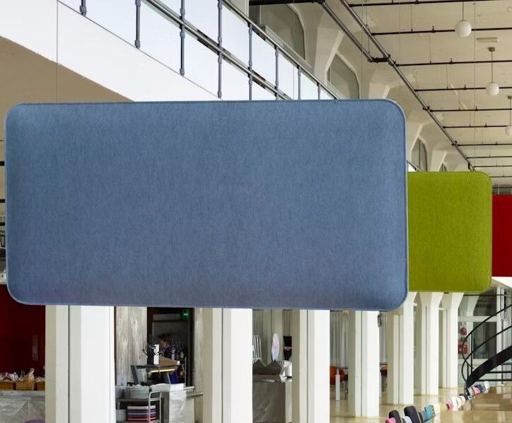 Zwei schallabsorbierende Paneele, eines blau und eines grün, hängen in einem modernen Bürogebäude.