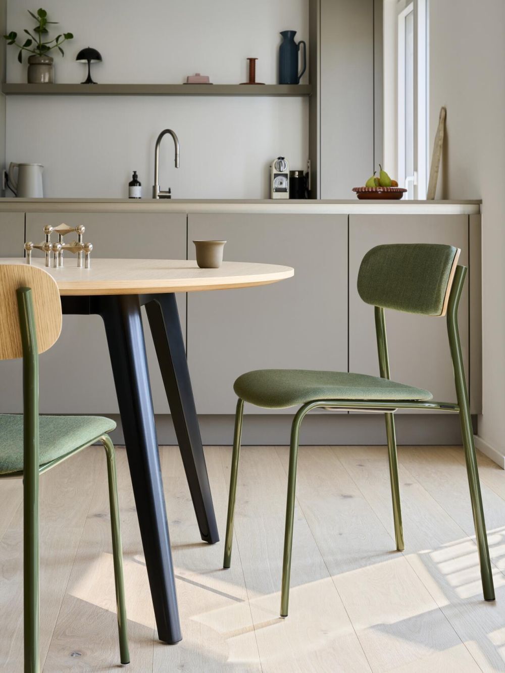 Moderner Essbereich mit grünem Stuhl, Holztisch und minimalistischer Küche im Hintergrund.