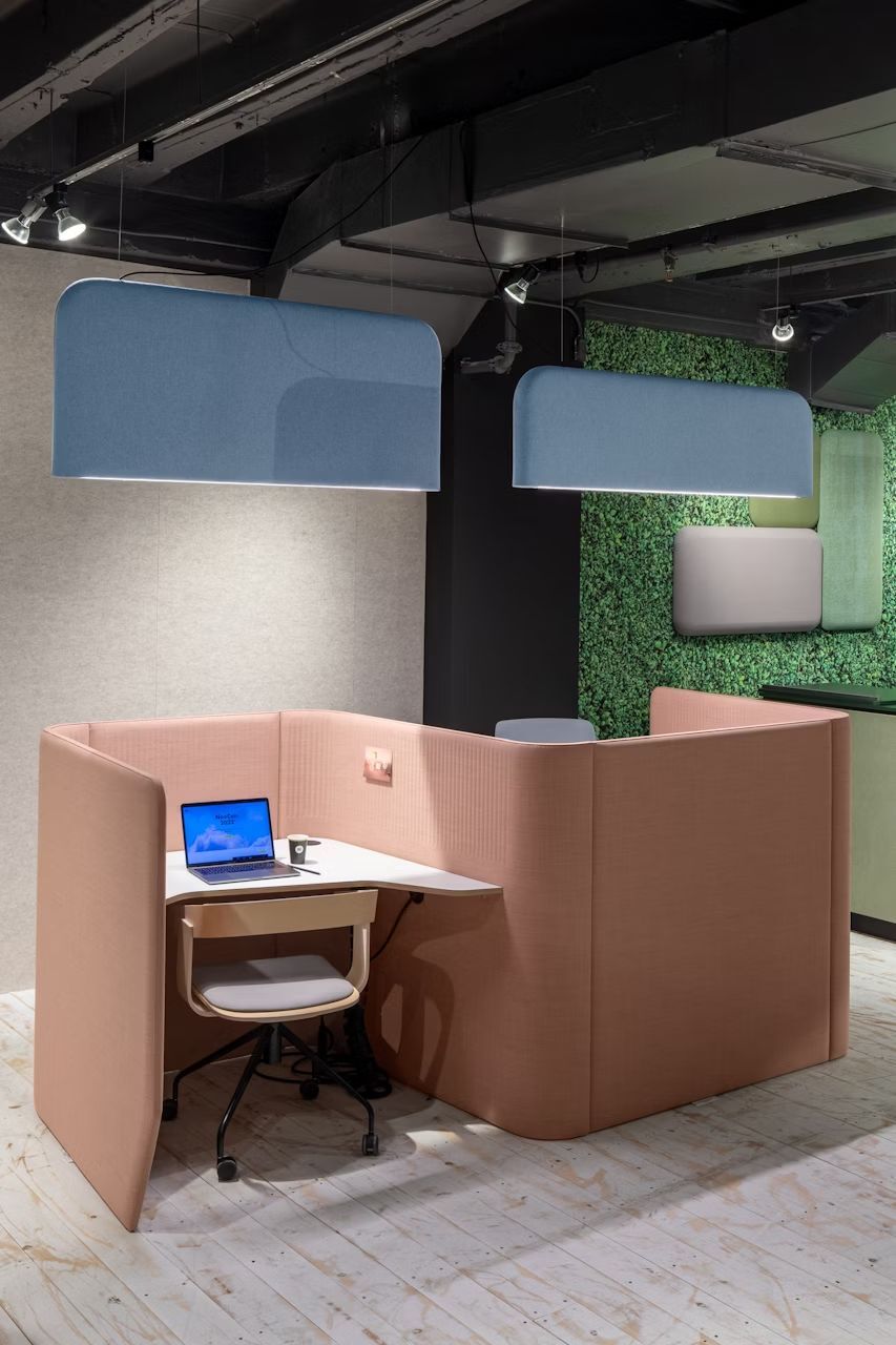 Moderne Bürokabine mit ergonomischem Stuhl und Laptop, umgeben von schallabsorbierenden Wandpaneelen und Deckenleuchten.