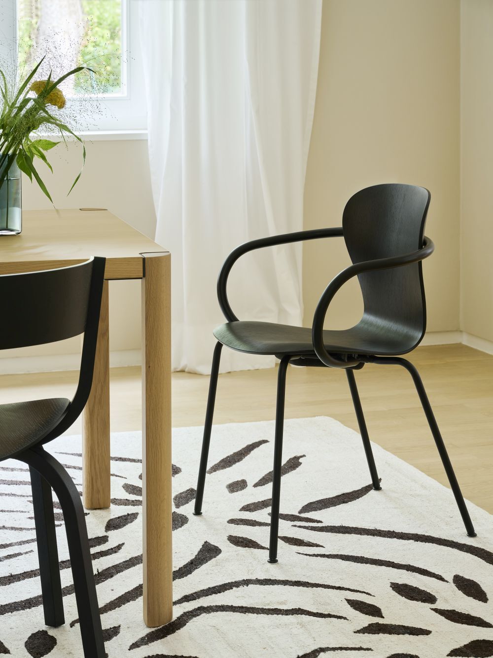 Moderner ergonomischer Stuhl mit gebogenem Rahmen vor einem Holztisch auf gemustertem Teppich in hellem Raum.