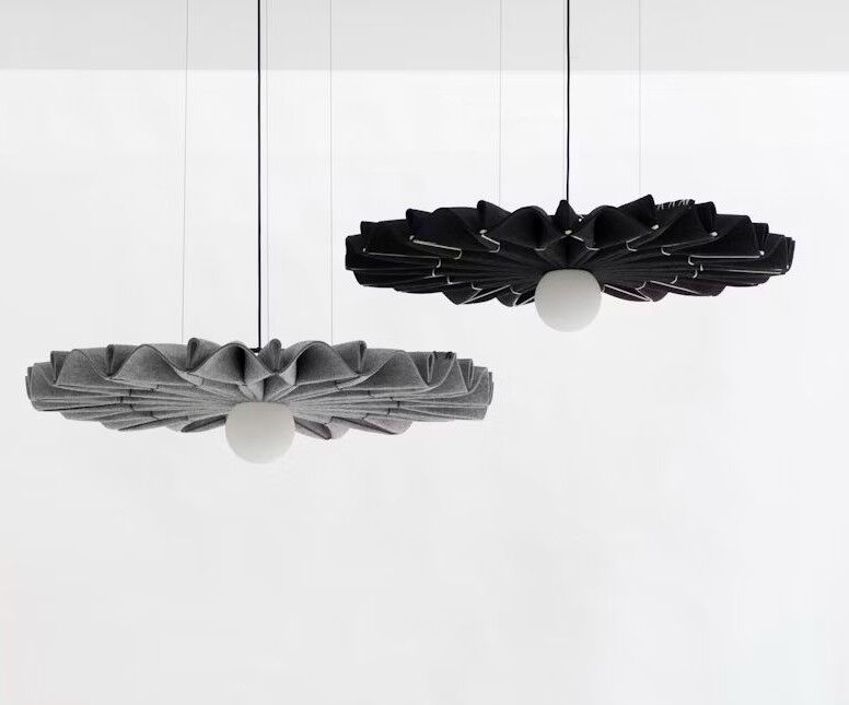Zwei hängende, moderne Lampen mit Faltendesign, eine in Grau, die andere in Schwarz, vor weißem Hintergrund.