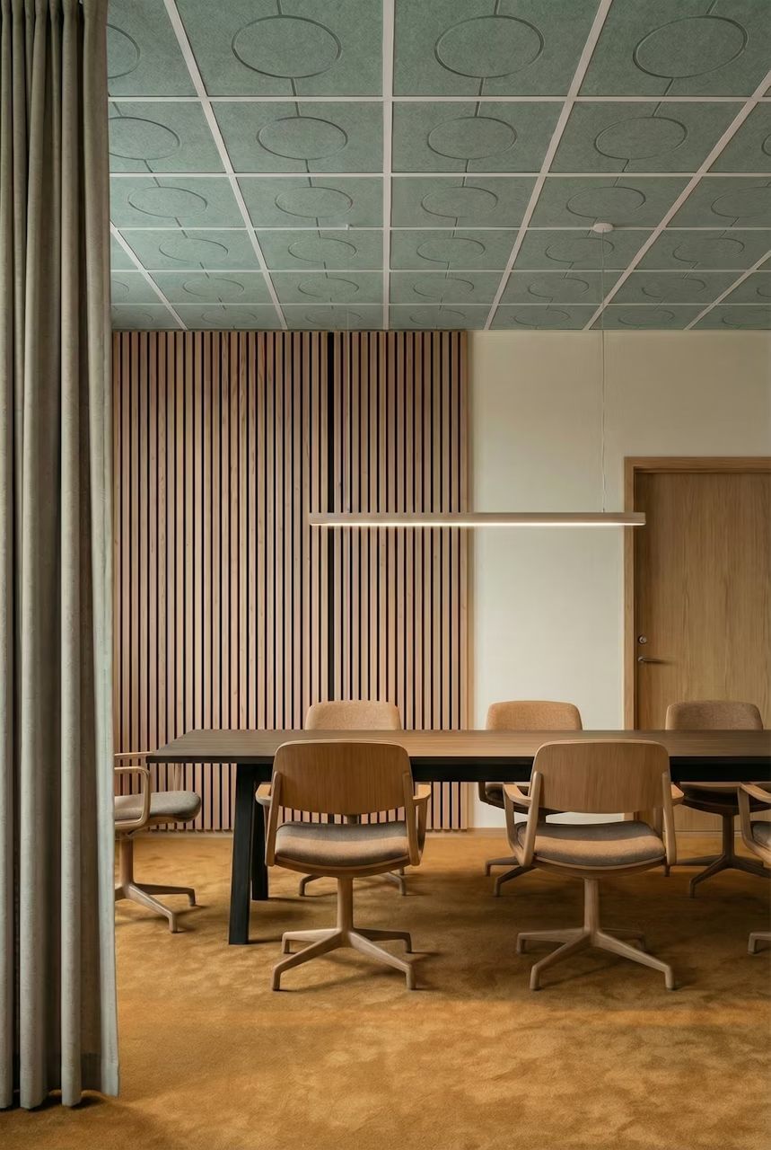 Moderner Konferenzraum mit ergonomischen Holzstühlen und langem Tisch auf flauschigem Teppichboden.
