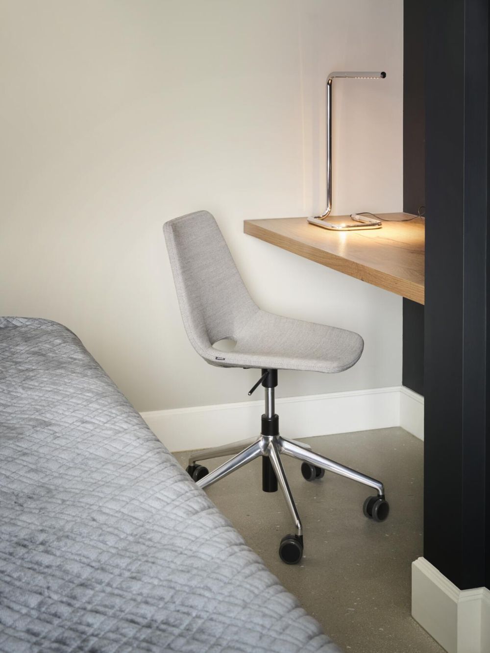 Moderner ergonomischer Bürostuhl neben einem Schreibtisch mit einer stilvollen Lampe in einer gemütlichen Ecke.